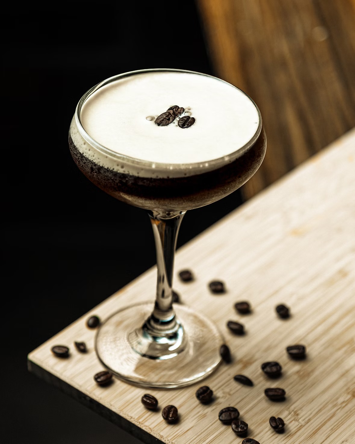 An espresso martini with coffee beans on the foam, its stem on a wooden board scattered with beans at O'Pub.